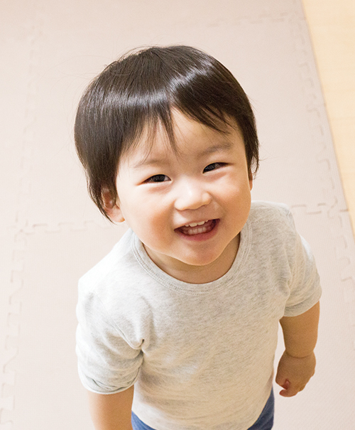 Smiling toddler standing indoors on a padded floor