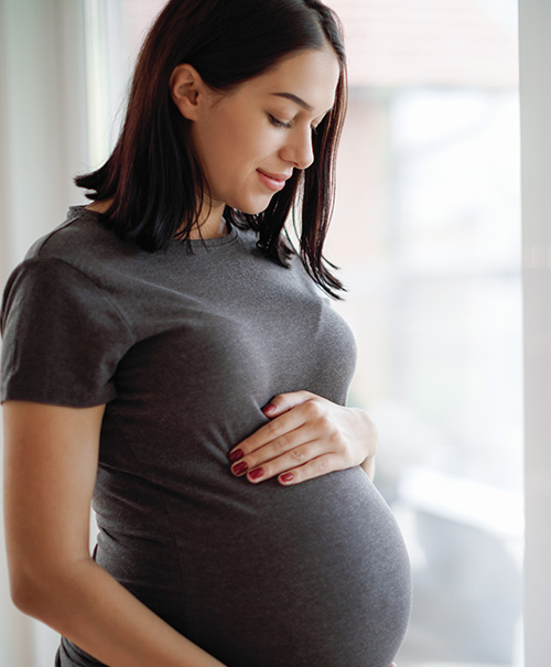 A pregnant woman enjoying the view while cradling her baby bump with a peaceful smile.